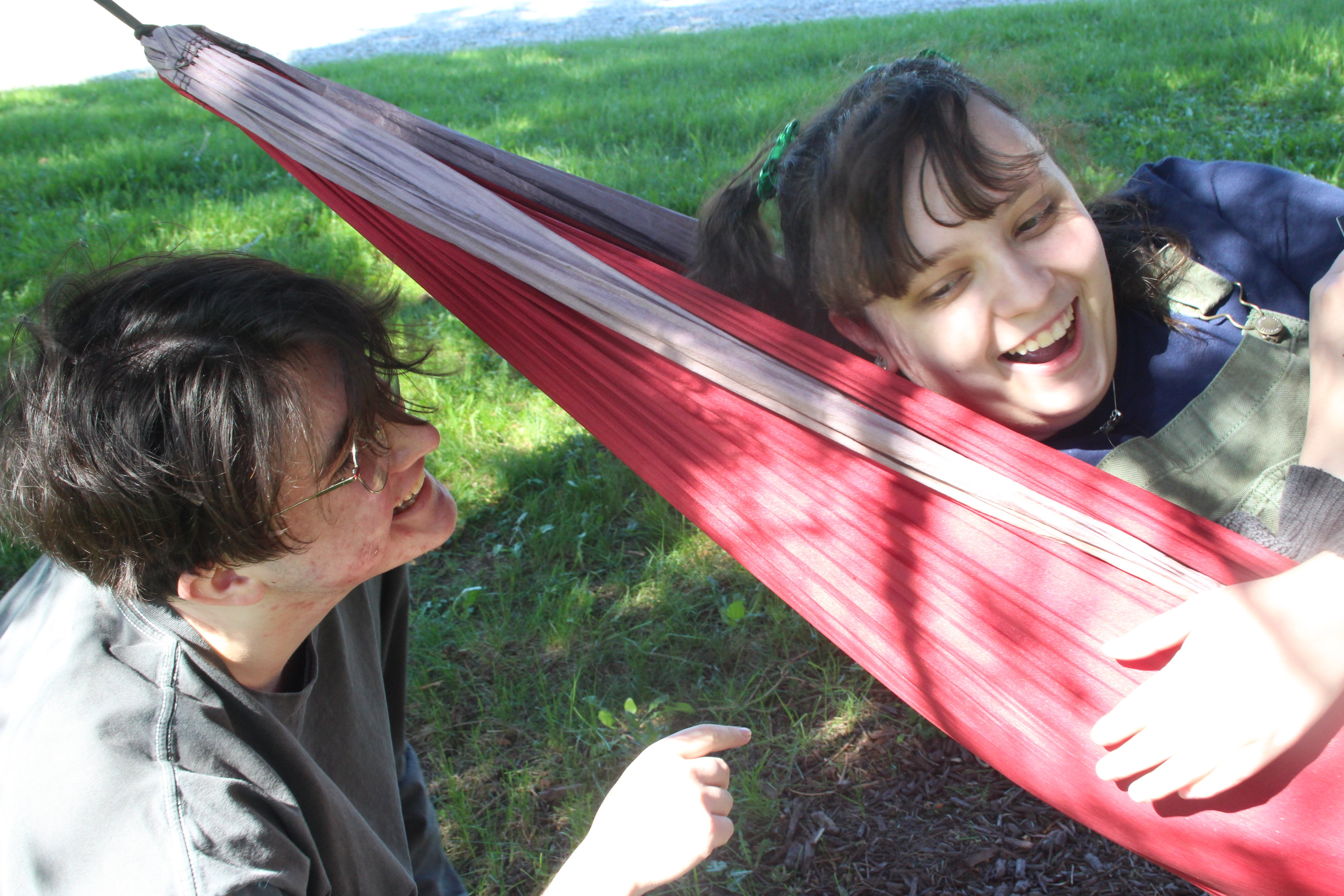 Two white people hanging out on a campus quad. The person on the right is in a pink hammock.